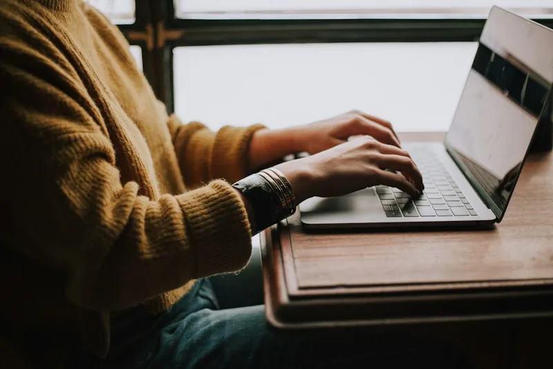 Marketeer typt op een laptop aan een houten tafel